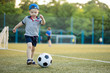 young little kid 3 or 5  years old enjoying happy playing football soccer at grass city park field posing smiling proud standing holding the ball in childhood sport passion and healthy lifestyle