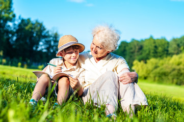 Wall Mural - Attractive grandmother with her grandson are learning school assignments outdoors together. A boy with a granny is studying for the summer holidays. Self-education and development