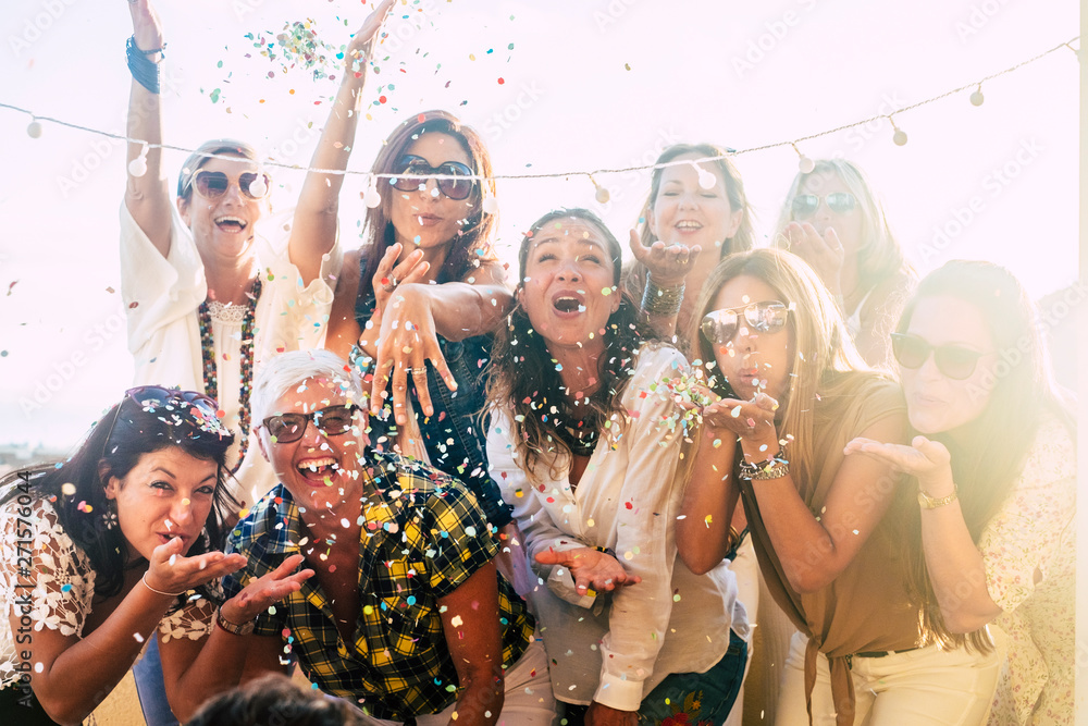 Group of people celebrate together having a lot of fun blowing coloured confetti - friendship and diversity ages generation laugh and smile on party - cheerful joyful concept for ladies - obrazy, fototapety, plakaty 