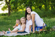 © illustrissima - Happy woman with her three kids sits on the plaid outdoor. Family picnic