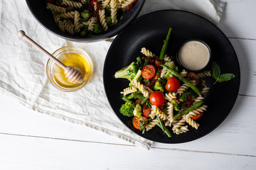 Wall Mural - Salad with pasta fusilli and vegetables in black bowl on white background. Top view flat lay.