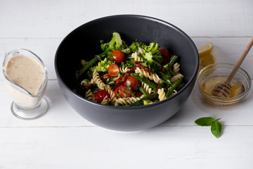 Wall Mural - Cold Italian salad with pasta and vegetables in black bowl on white background.