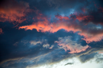 Wall Mural - A stormy sky with a bright red glow. Colorful image of dramatic cloudscape. Amazing clouds of pink, white, gray color on the background of the evening dark sky after sunset.