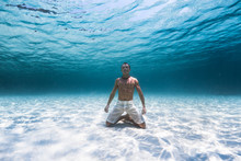 Young Muscular Man Stands On The Knees On The Sandy Sea Bottom In A Relaxed Pose
