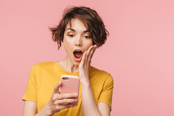 Shocked young beautiful woman posing isolated over pink wall background using mobile phone.