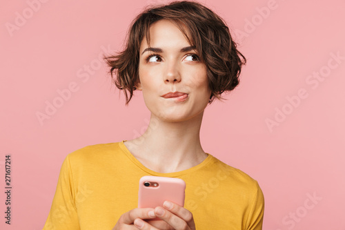 Fotografía Thinking dreaming young beautiful woman posing isolated over pink wall background using mobile phone
