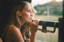 Mood Atmospheric Lifestyle Portrait Of Young Beautiful Blonde Hair Girl Looking Out Of Window From Riding Train. Pretty Teen Enjoying Beauty Of Nature From Moving Train Car In Summer. Travel Concept