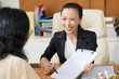 © DragonImages - Asian social worker smiling and suggesting the woman to sign a contract while they siting at office