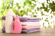 Stack of clean towels with detergents on table against blurred background. Space for text