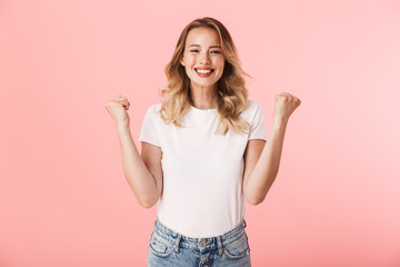 Poster - Happy young blonde woman posing isolated over pink wall background make winner gesture.