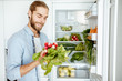 © rh2010 - Young vegan man choosing what to cook, taking fresh vegetables from the refrigerator at home