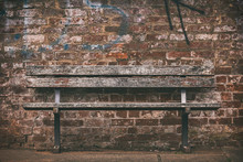Old Wooden Bench Against A Brick Wall With Graffiti.