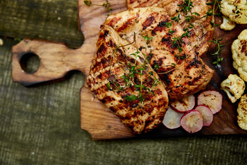 Wall Mural - Grilled turkey meat. Steak turkey grill on wooden cutting board with a variety of grilled vegetables on  rustic background  Top view. Flat lay. Copy space..