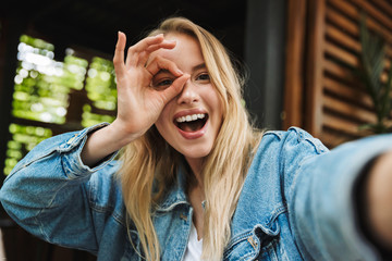 Wall Mural - Amazing excited happy young woman posing outdoors in cafe take a selfie by camera.