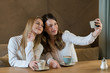 © Alvaro Hernandez/ADDICTIVE STOCK - Two stylish female friends with cups of fresh coffee smiling and posing for selfie while sitting at table in cozy restaurant
