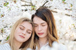 © Alvaro Hernandez/ADDICTIVE STOCK - Two dreamy young women with closed eyes near trees with white flowers on sunny day in park