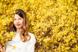 © Alvaro Hernandez/ADDICTIVE STOCK - Attractive lady smiling and looking at camera while standing near tree branches blooming with yellow flowers