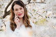 © Alvaro Hernandez/ADDICTIVE STOCK - Young woman smiling and talking over the phone near trees with white flowers on sunny day in park looking at camera