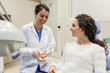 © David Fuentes/ADDICTIVE STOCK - Happy young female stomatologist sitting in dental cabinet. showing dummy jaw to joyful young woman and laughing
