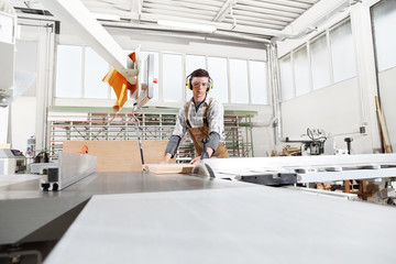 carpenter man work in the carpentry, cut a wooden board with circular saw machine, protected with ear muffs and glasses