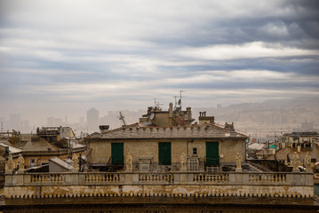 Wall Mural - View of Genoa rooftops with the top of Bendinelli Sauli palace (16th century) in the foreground and the fogged skyline silhouette in the background in a rainy day with cloudy sky, Liguria, italy