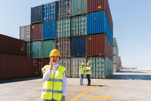 Female Worker On The Phone In Front Of Colleagues And Cargo Containers On Industrial Site