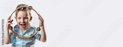 Fotomural a cheerful boy in a blue shirt holding a tambourine and smiling on a light backg
