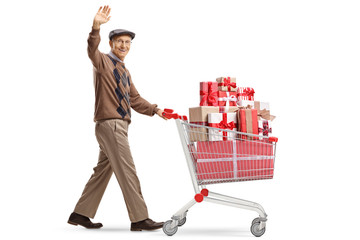 Wall Mural - Cheerful elderly man with a shopping cart full of presents waving at the camera