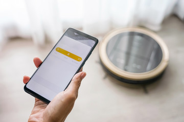 Woman holding smartphone using mobile application to control robotic vacuum cleaner for Start Cleaning