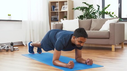 Wall Mural - sport, technology and healthy lifestyle concept - indian man using fitness tracker and doing plank exercise at home