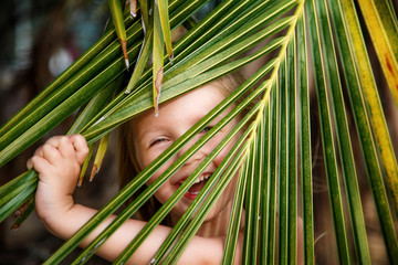 Portrait of happy little girl with palm leaf. Summer vacations concept, tropical vibes. Kid smiling.