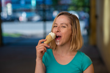 Portrait of a cute girl in a green dress is walking outside and eating dessert. Beautiful blonde enjoying a cone with ice cream on a beautiful summer day. Life is a pleasure