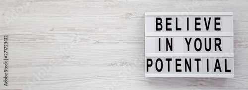 Fotomural Top view, 'Believe in your potential' words on a lightbox on a white wooden surface