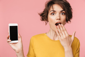 Shocked young beautiful woman posing isolated over pink wall background using mobile phone.
