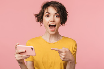 Shocked young beautiful woman posing isolated over pink wall background play games by mobile phone.