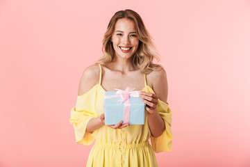 Poster - Happy young blonde woman posing isolated over pink wall background holding present gift box.