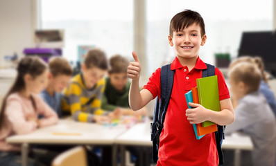 Wall Mural - education and people concept - smiling little student boy in red polo t-shirt in glasses with books and bag showing thumbs up over school class background
