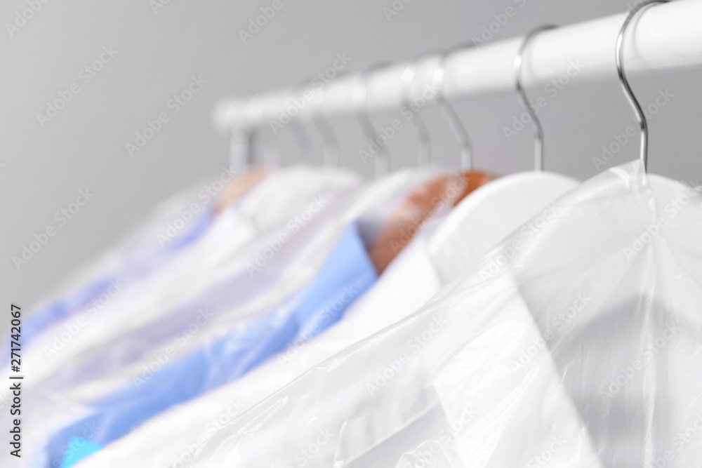 Rack with clothes after dry-cleaning on light background, closeup