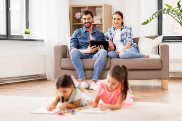 Sticker - family, leisure and people concept - happy mother and father with tablet pc computer sitting on sofa and looking at daughters drawing at home