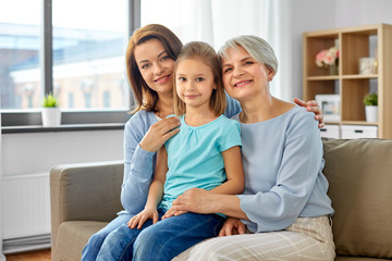 Canvas Print - family, generation and female concept - portrait of smiling mother, daughter and grandmother sitting on sofa at home