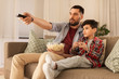 © Syda Productions - family, childhood, fatherhood, technology and people concept - father and little son with popcorn and remote control watching tv at home in evening