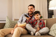 © Syda Productions - family, childhood, fatherhood, technology and people concept - happy father and little son with popcorn and remote control watching tv at home in evening