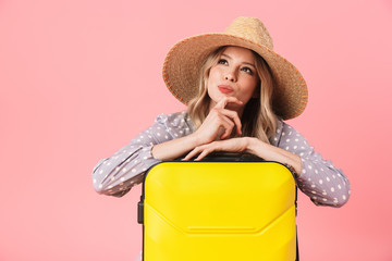 Thinking young pretty woman tourist posing isolated over pink wall background with suitcase.