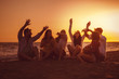 © djile - Happy friends sitting on the beach singing and playing guitar during the sunset