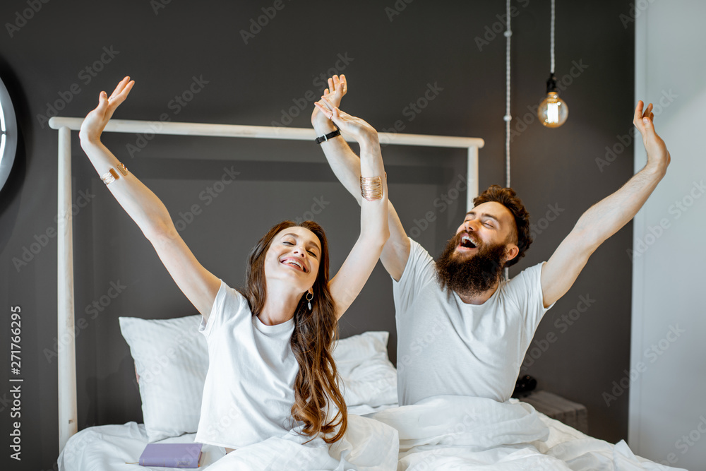 Happy couple waking up with raised hands, feeling good in the morning at home - obrazy, fototapety, plakaty 
