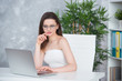 © Yarkovoy - A young brunette girl with glasses in a white dress is sitting in the office at the table. Woman works at the laptop. Low vision or fashion accessory