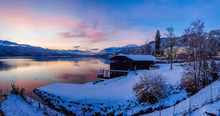 Beautiful View On Millstätter Lake In Austria. The Lake Is Surrounded By Alps. Mountains Are Covered With Snow. The Sky Is Exploding With Pink And Orange. Stunning Sunset. Little Cottage On The Side.