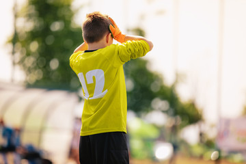 Sad junior soccer goalkeeper. Disappointed boy in yellow goalie sportswear kit with hands on his head. Junior youth football team loosing goal