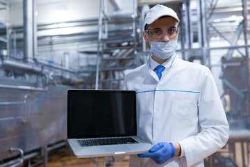 Wall Mural - Portrait of man in a white robe and a cap standing in production department of dairy factory with laptop