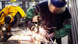 Heavy industry worker cutting steel with grinder machine in industrial manufacture, wearing safety equipments